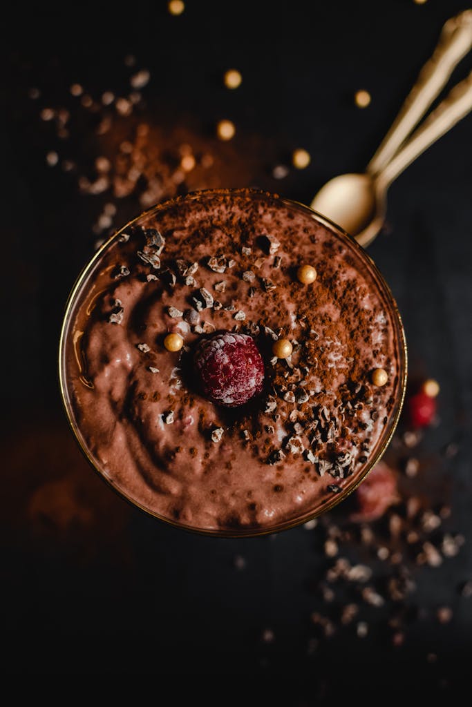 Delicious chocolate mousse topped with raspberry and gold pearls on a dark background.