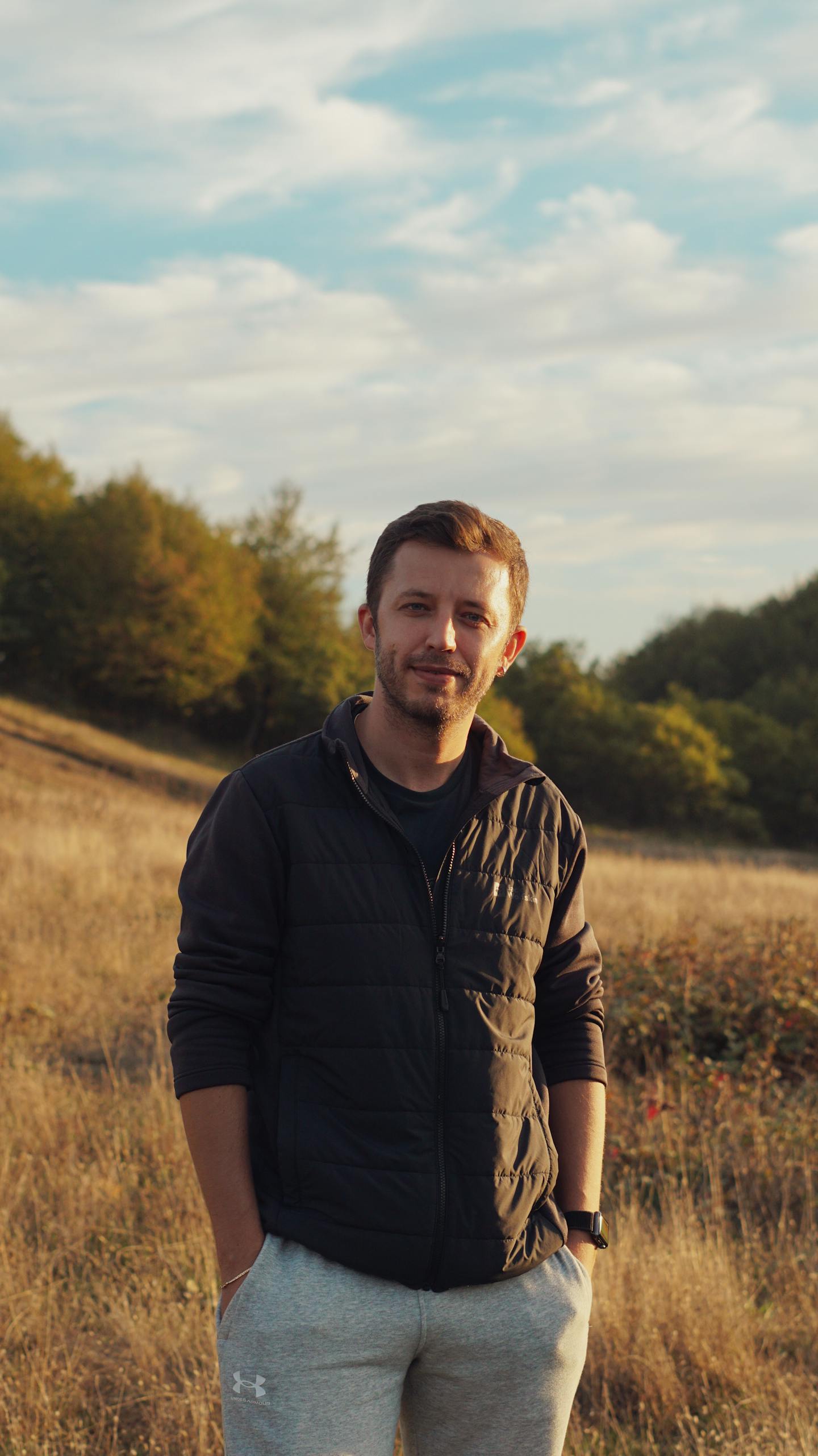 Portrait of a man standing in a grassy field during a warm autumn day.